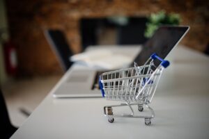 Keranjang belanja mini di samping laptop sebagai gambaran transaksi belanja daring