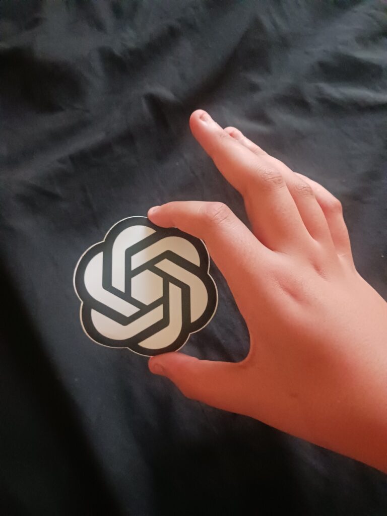 Tangan memegang stiker lambang OpenAI, simbol pemakaian ChatGPT